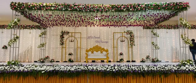 Overhead floral canopy with hanging rose garland strings above a gold bridal sofa, sheer white drapes with warm fairy lights, gold arch frames and chandeliers from Joy Events & Catering's past décor