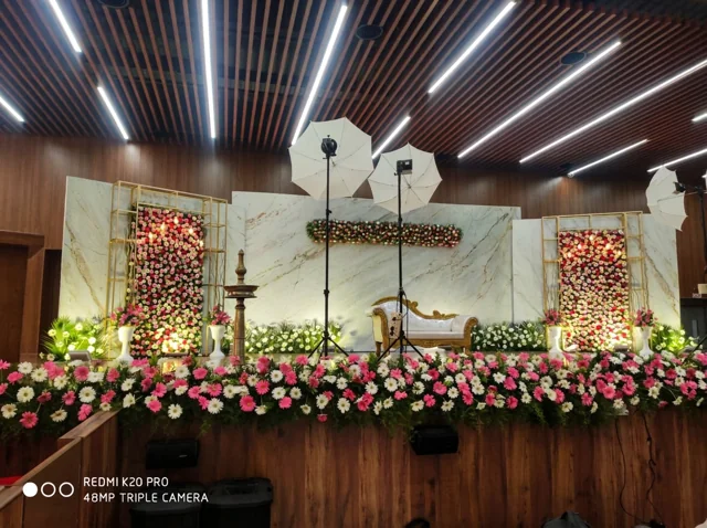 Marble-look backdrop with gold-framed floral panels, ornate white and gold sofa and a brass lamp, photographed with lighting equipment during a past Joy Events & Catering setup