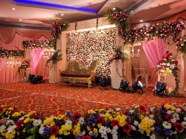 Ornate gold bridal sofa in front of a flower wall with pink drapes, hanging chandeliers and floral arrangements from Joy Events & Catering's past décor work