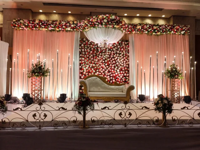 Peach drapes around a central red and white flower wall, white and gold sofa, overhead fabric canopy and tall candle-style lights from Joy Events & Catering's past décor