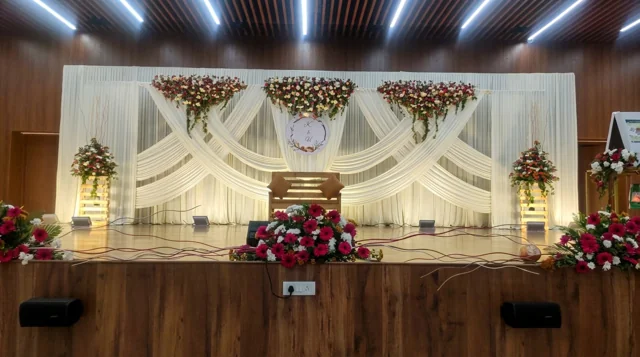 Crossed ivory fabric swags with red and white floral clusters, wooden bridal seating and lit flower stands in a past Joy Events & Catering stage design